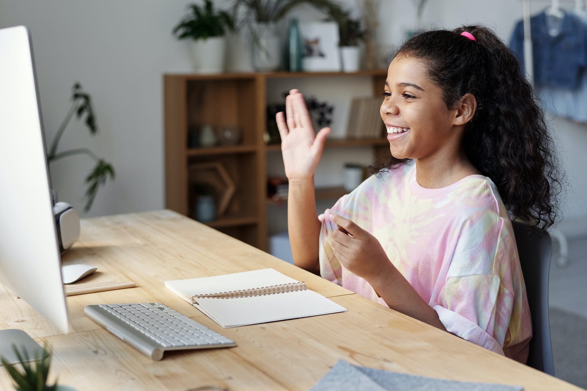 Smiling girl waves to online teacher in a fun online class.